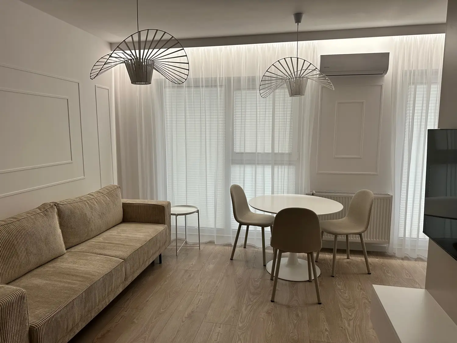 Jasny salon z sofą, okrągłym stołem i dużymi oknami